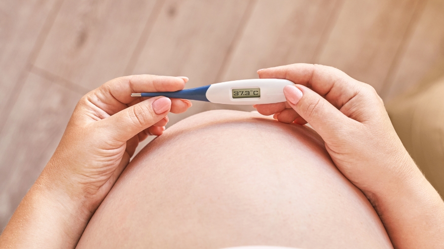 Brzuch ciążowy, a przed nim termometr