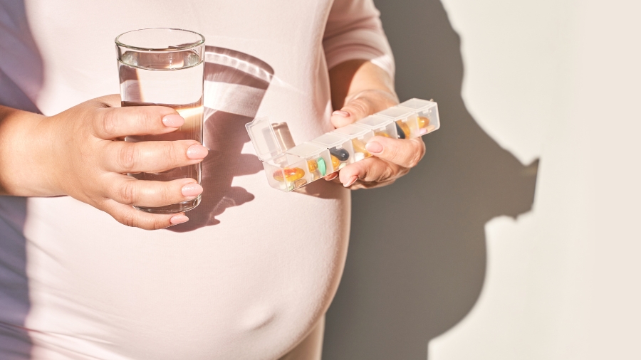 Kobieta w ciąży z pill boxem oraz szklanką wody